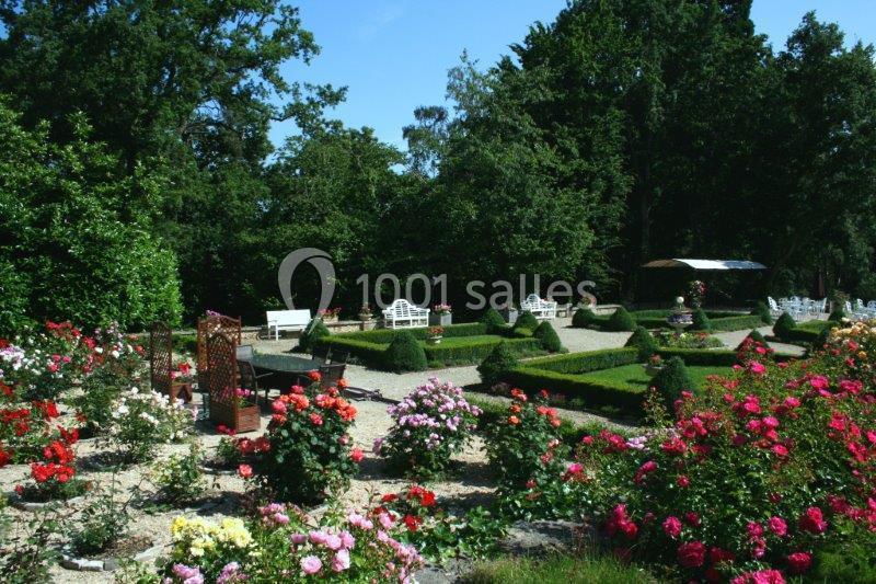 Jardin fleuri avec parterres de roses colorées, allées gravillonnées et bancs entourés de verdure.