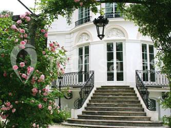 Façade d'une maison blanche avec escalier en pierre, balustrades en fer forgé et rosiers en fleurs au premier plan.