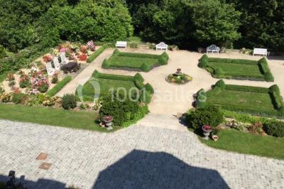 Allée bordée d'arbustes menant à une grande maison entourée d'arbres, capturée en noir et blanc.