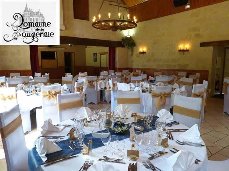 Salle de réception décorée avec des tables rondes dressées, nappes blanches et chaises ornées de rubans dorés.
