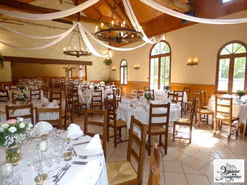 Salle de réception lumineuse avec tables dressées, chaises en bois et décoration suspendue sous un plafond en poutres…