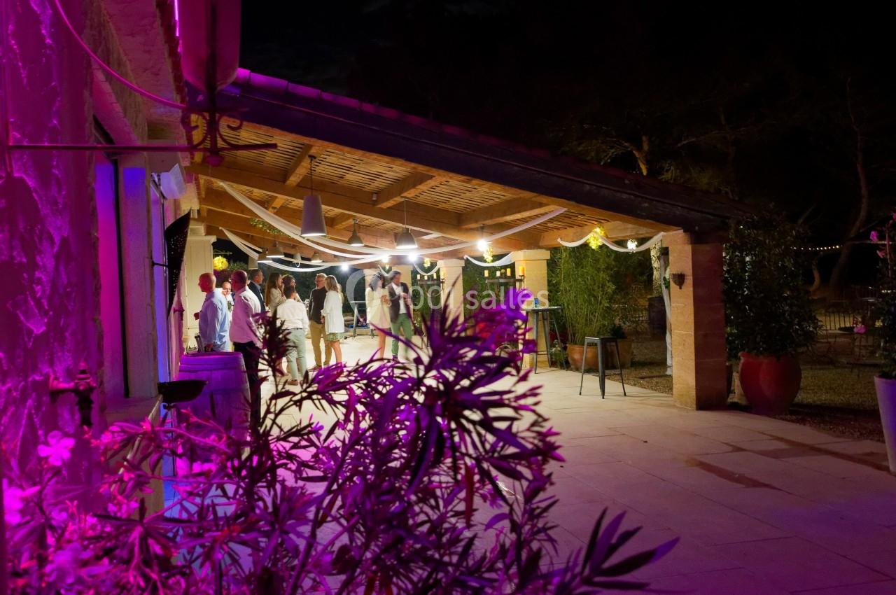 Terrasse éclairée en soirée avec des invités discutant sous un auvent décoré, entourée de végétation.