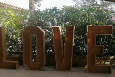 Cour extérieure ensoleillée avec des plantes en pots, des chaises en métal et un bâtiment à toit de tuiles en arrière-plan.