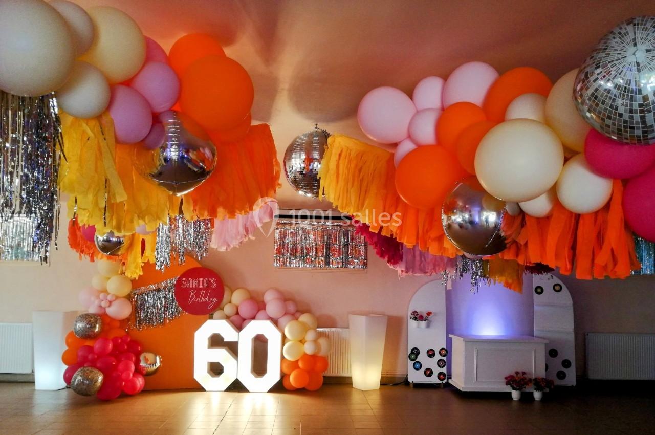 Décoration festive avec ballons colorés, guirlandes et chiffres lumineux ’60’ dans une salle de réception.