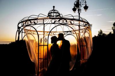 Cour extérieure ensoleillée avec des plantes en pots, des chaises en métal et un bâtiment à toit de tuiles en arrière-plan.