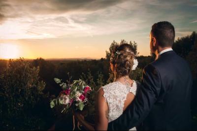 Cour extérieure ensoleillée avec des plantes en pots, des chaises en métal et un bâtiment à toit de tuiles en arrière-plan.