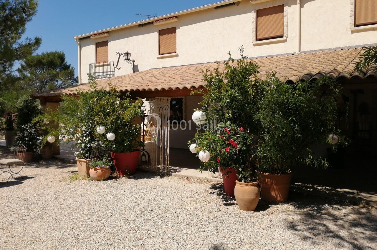 Façade d'une maison méditerranéenne avec terrasse ombragée, pots de fleurs et lanternes décoratives.