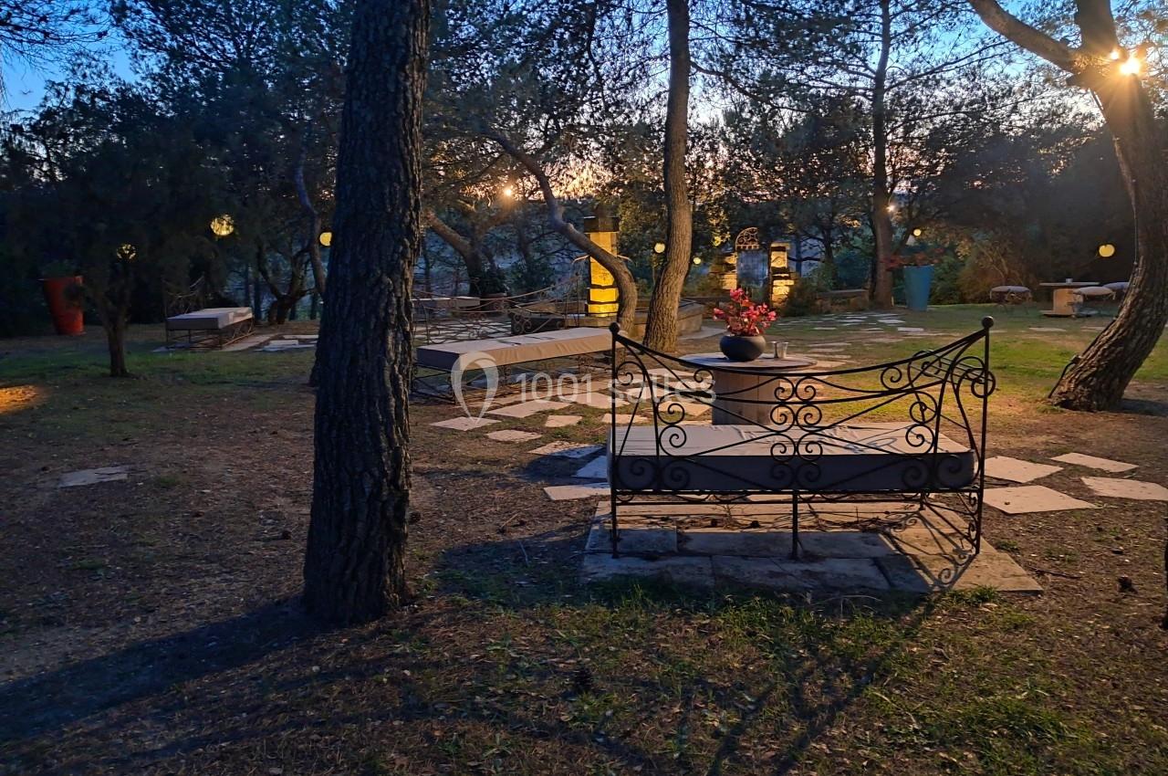 Banc en fer forgé dans un jardin boisé éclairé par des lampes suspendues au crépuscule.