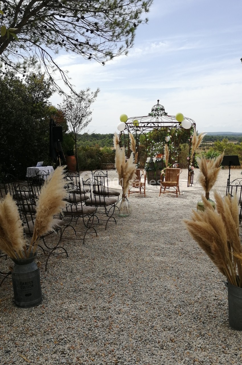 Chaises disposées en extérieur face à une pergola décorée, entourée de végétation et de bouquets d'herbes de la pampa.