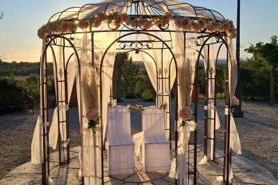 Cour extérieure ensoleillée avec des plantes en pots, des chaises en métal et un bâtiment à toit de tuiles en arrière-plan.