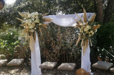 Cour extérieure ensoleillée avec des plantes en pots, des chaises en métal et un bâtiment à toit de tuiles en arrière-plan.