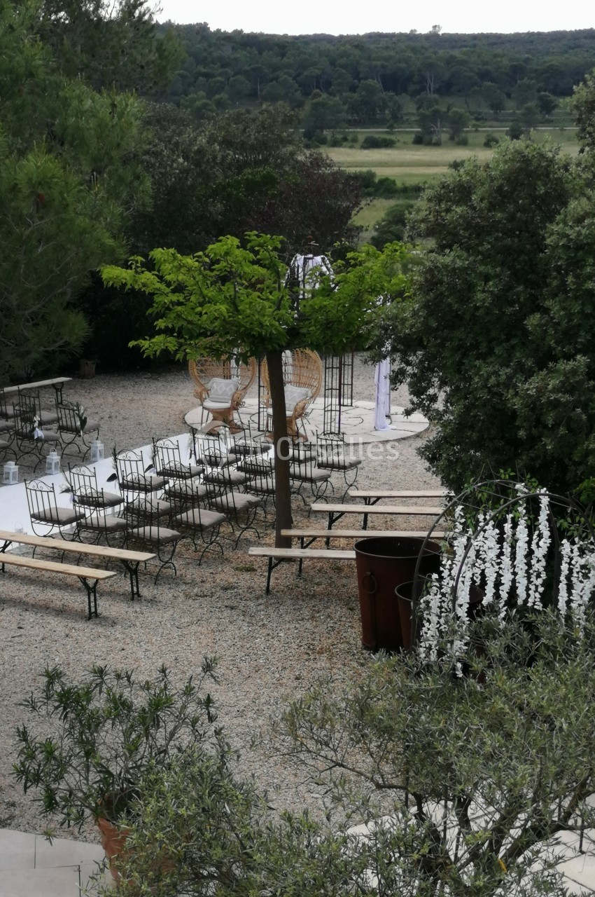 Espace extérieur aménagé avec des bancs, des chaises et des arbres, entouré de verdure et de décorations florales.