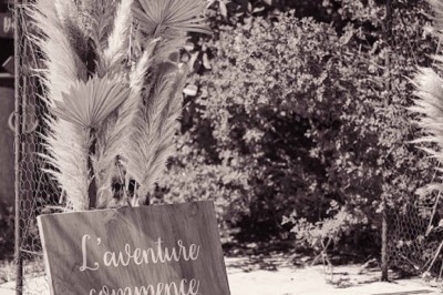 Cour extérieure ensoleillée avec des plantes en pots, des chaises en métal et un bâtiment à toit de tuiles en arrière-plan.