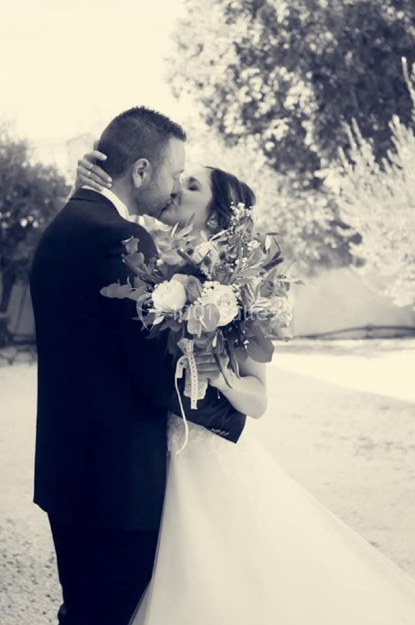 Un couple en tenue de mariage s'embrasse tendrement, la mariée tenant un bouquet de fleurs.
