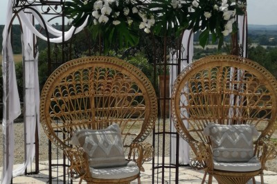 Cour extérieure ensoleillée avec des plantes en pots, des chaises en métal et un bâtiment à toit de tuiles en arrière-plan.