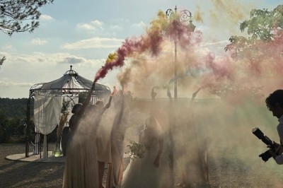 Cour extérieure ensoleillée avec des plantes en pots, des chaises en métal et un bâtiment à toit de tuiles en arrière-plan.