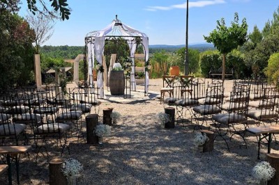 Cour extérieure ensoleillée avec des plantes en pots, des chaises en métal et un bâtiment à toit de tuiles en arrière-plan.