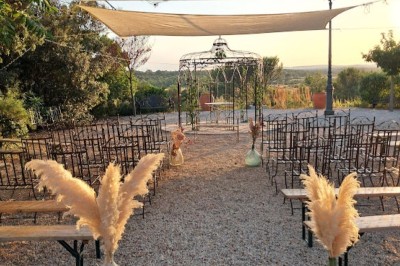 Cour extérieure ensoleillée avec des plantes en pots, des chaises en métal et un bâtiment à toit de tuiles en arrière-plan.
