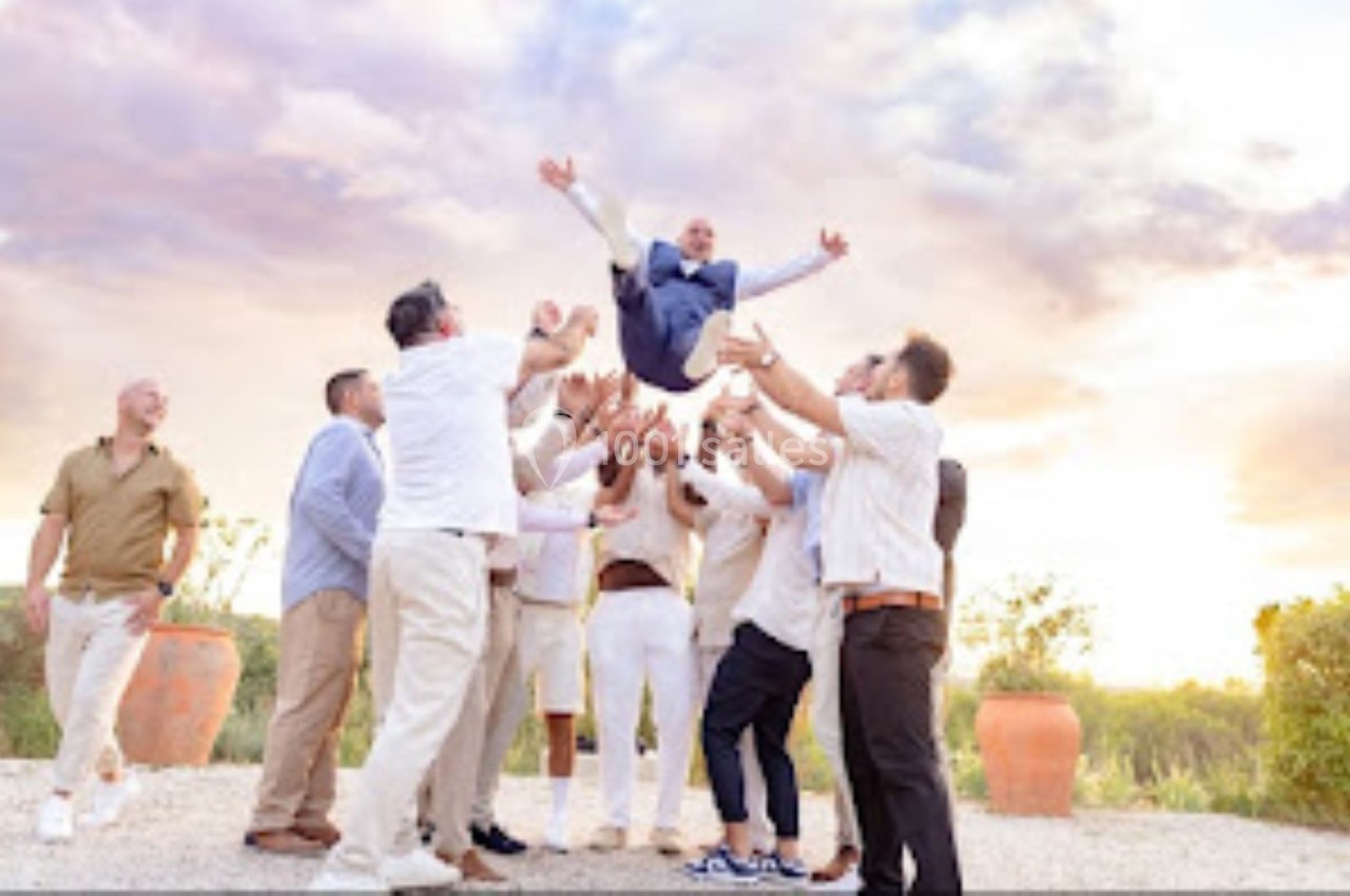 Un groupe d'hommes lance en l'air une personne en costume dans un cadre extérieur au coucher du soleil.