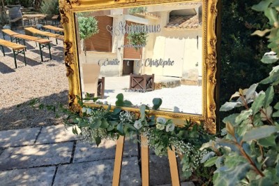 Cour extérieure ensoleillée avec des plantes en pots, des chaises en métal et un bâtiment à toit de tuiles en arrière-plan.