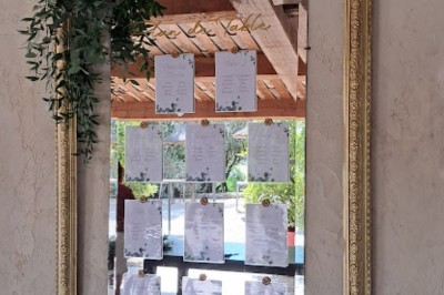 Cour extérieure ensoleillée avec des plantes en pots, des chaises en métal et un bâtiment à toit de tuiles en arrière-plan.