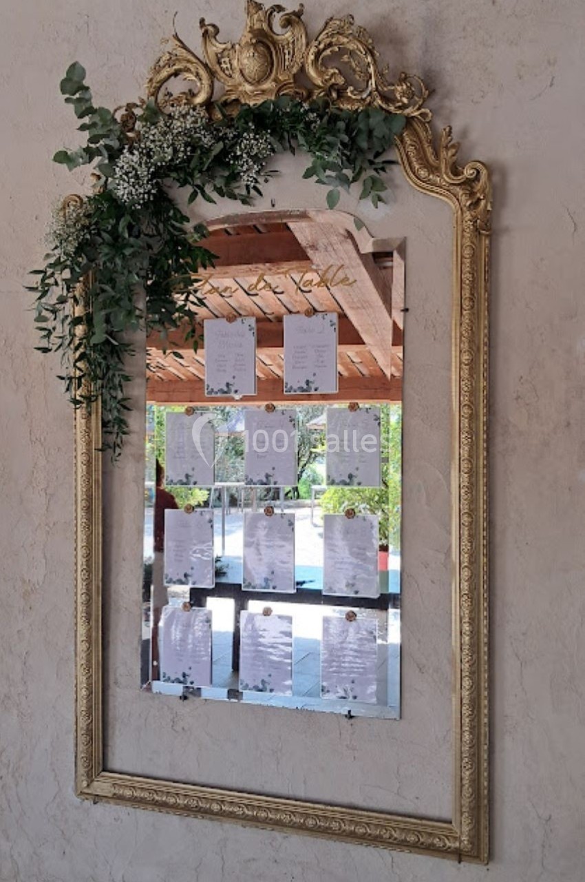 Miroir doré orné de feuillage et fleurs, reflétant des feuilles affichées et un espace extérieur lumineux.