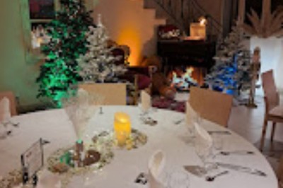 Table décorée pour une fête avec bougies, paillettes, centre de table lumineux et sapins illuminés en arrière-plan.