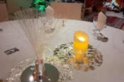 Table décorée pour une fête avec bougies, paillettes, centre de table lumineux et sapins illuminés en arrière-plan.