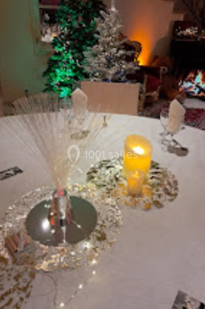 Table décorée pour une fête avec bougies, paillettes, centre de table lumineux et sapins illuminés en arrière-plan.
