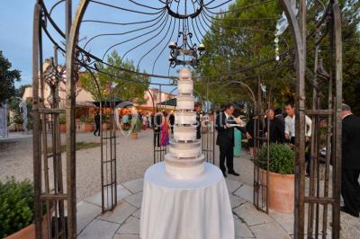 Cour extérieure ensoleillée avec des plantes en pots, des chaises en métal et un bâtiment à toit de tuiles en arrière-plan.