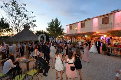 Cour extérieure ensoleillée avec des plantes en pots, des chaises en métal et un bâtiment à toit de tuiles en arrière-plan.