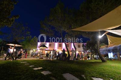 Cour extérieure ensoleillée avec des plantes en pots, des chaises en métal et un bâtiment à toit de tuiles en arrière-plan.