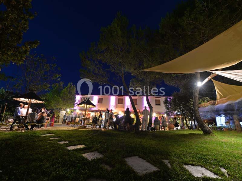 Un jardin éclairé de nuit avec des invités rassemblés près d'un bâtiment illuminé et des arbres environnants.