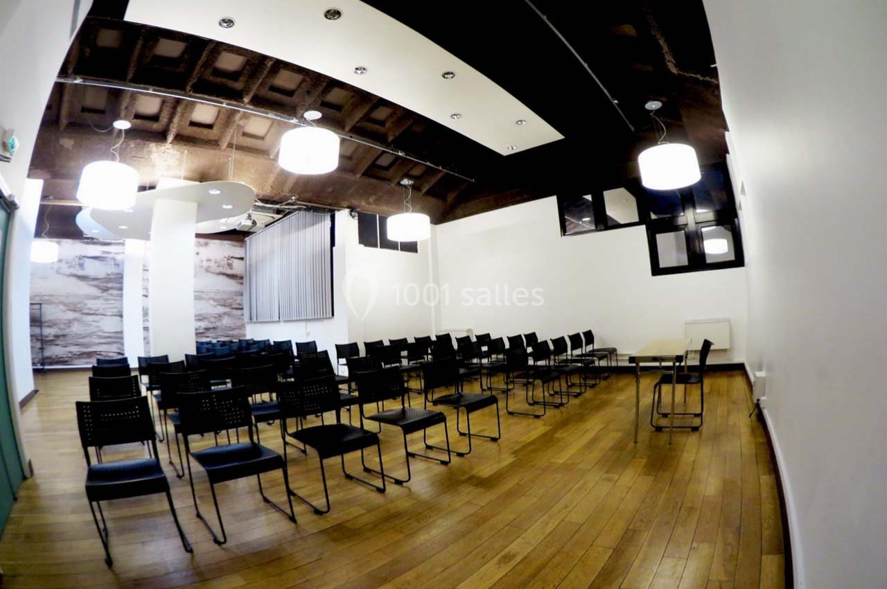 Salle de réunion vide avec des chaises noires alignées, parquet en bois et éclairage suspendu moderne.