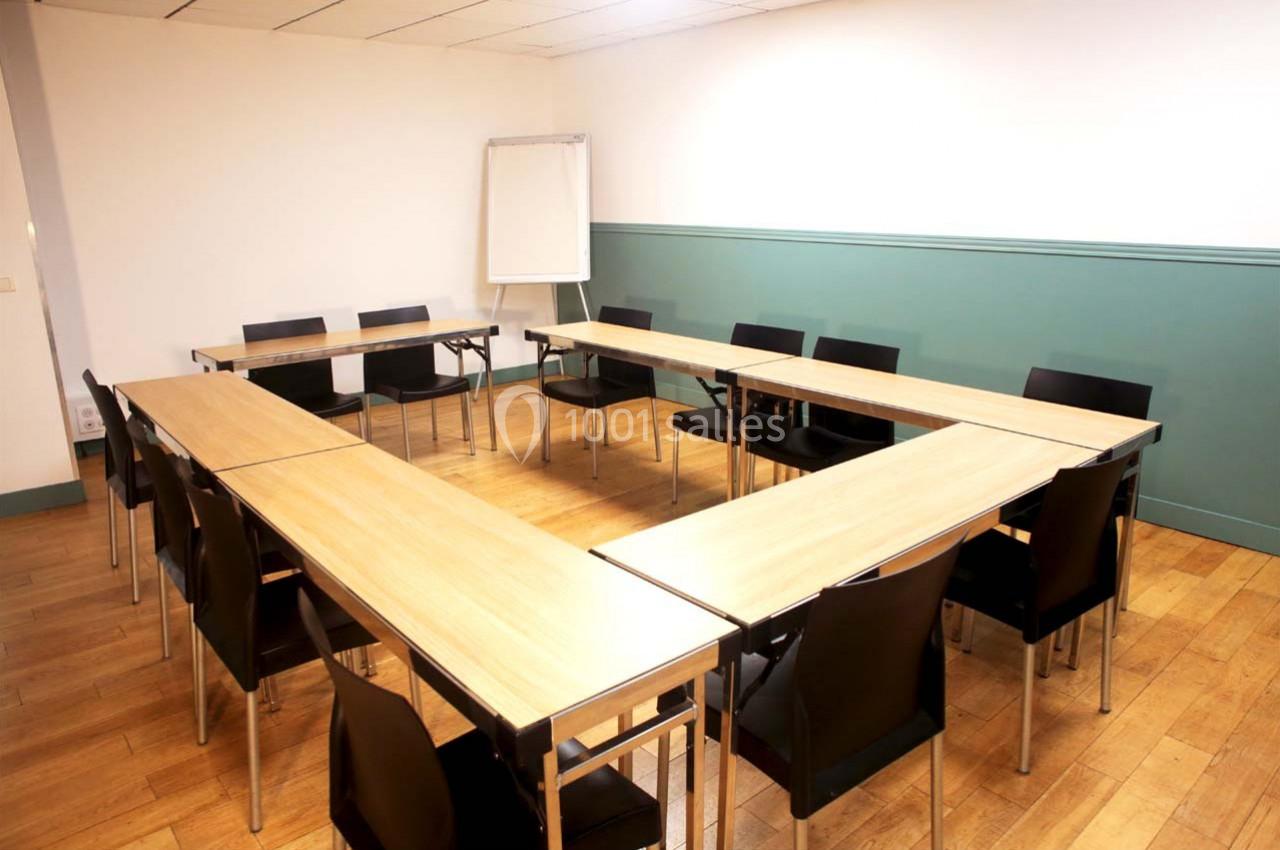 Salle de réunion avec tables disposées en U, chaises noires et tableau blanc sur un sol en bois clair.