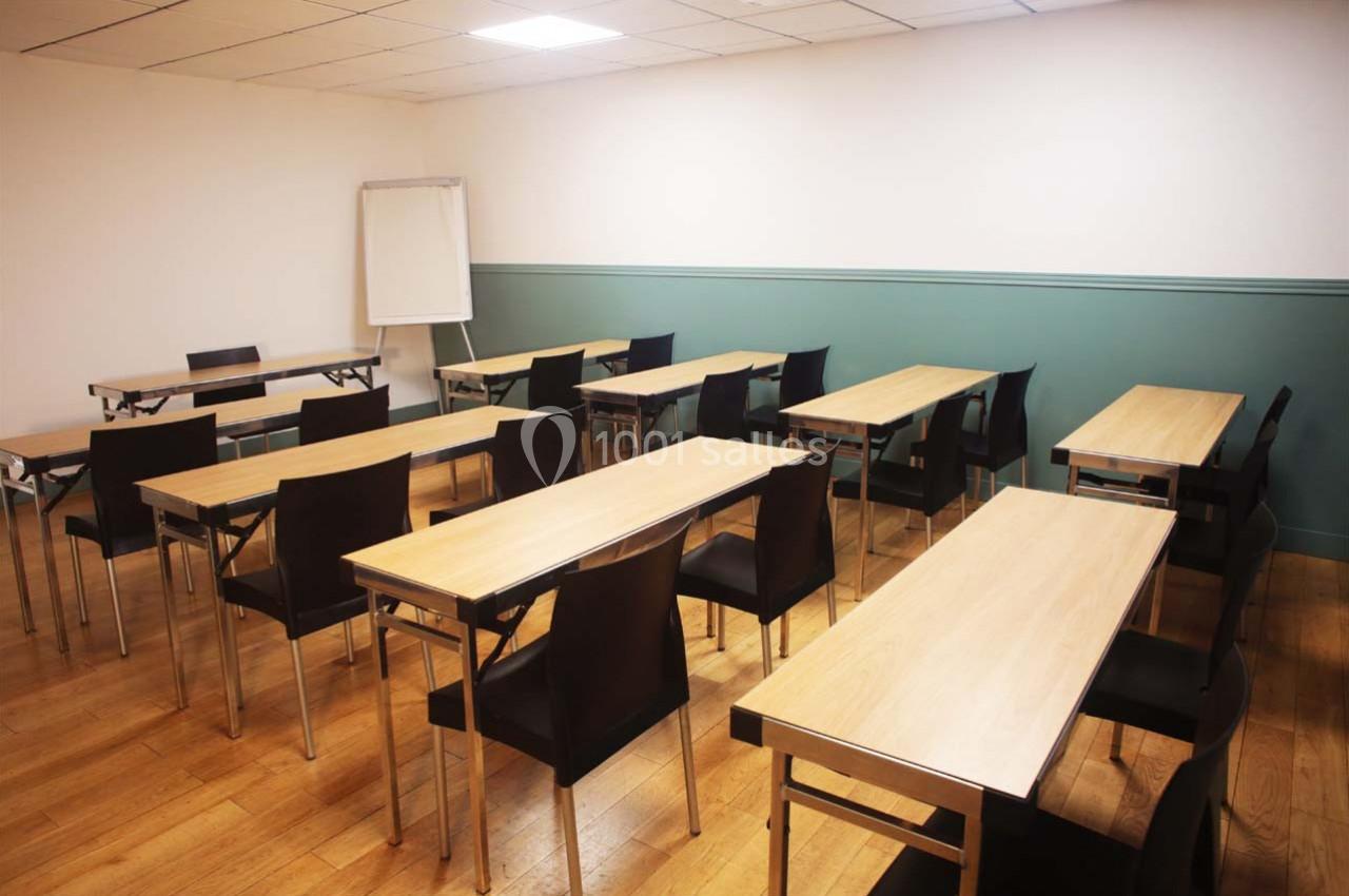 Salle de formation avec des tables en bois, des chaises noires et un tableau blanc dans un coin.