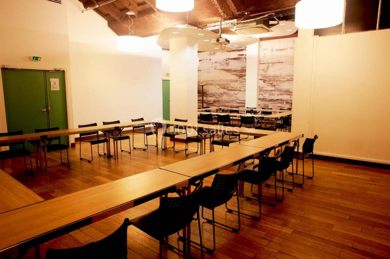 Salle de réunion lumineuse avec tables disposées en U, chaises noires et parquet en bois clair.