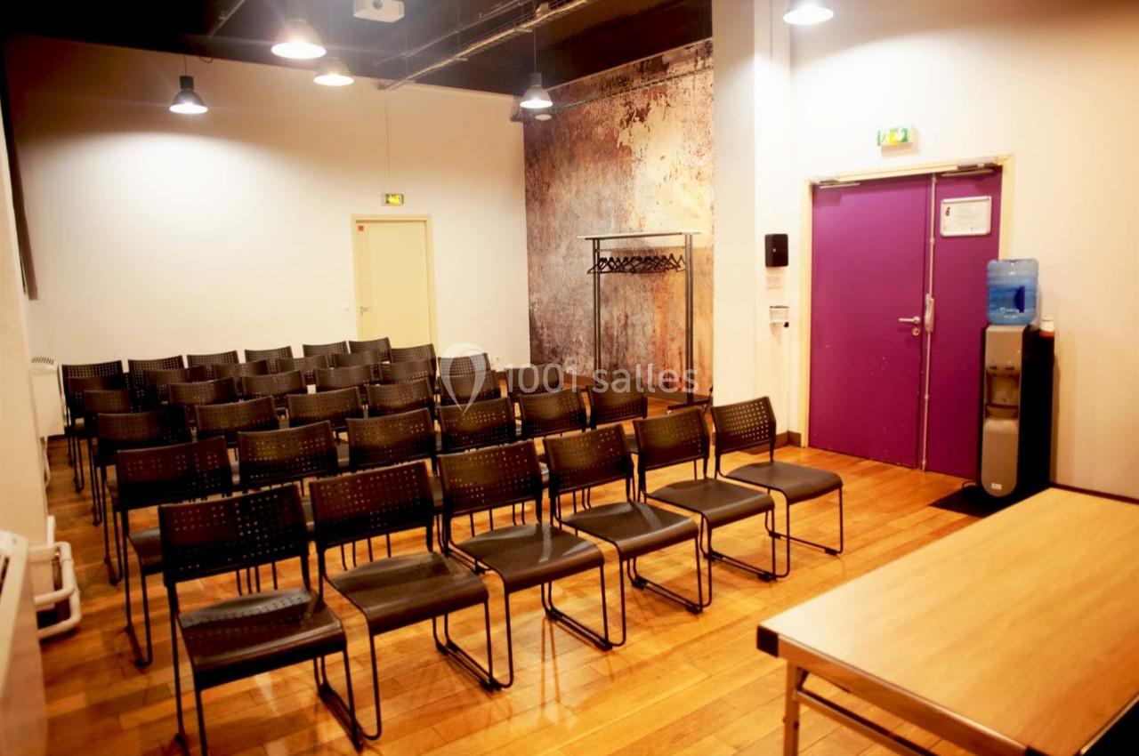 Salle de réunion avec rangées de chaises noires, table en bois au premier plan et porte violette en arrière-plan.