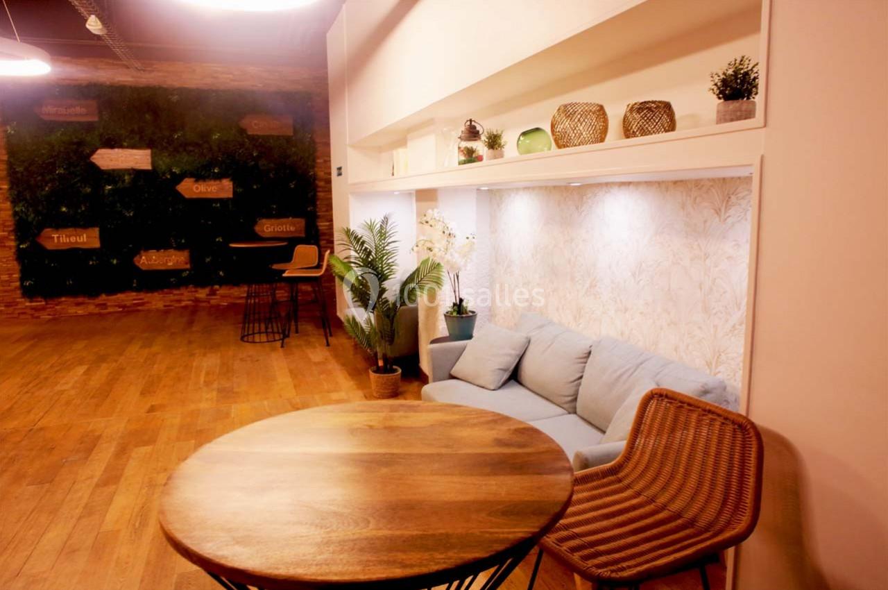 Espace intérieur avec table ronde en bois, canapé bleu, chaise en rotin et mur végétal en arrière-plan.