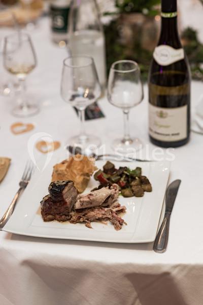 Assiette de viande rôtie avec garniture de légumes et feuilleté, servie sur une table dressée avec vin et verres.