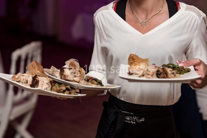 Une serveuse portant plusieurs assiettes garnies de plats variés dans un cadre intérieur.
