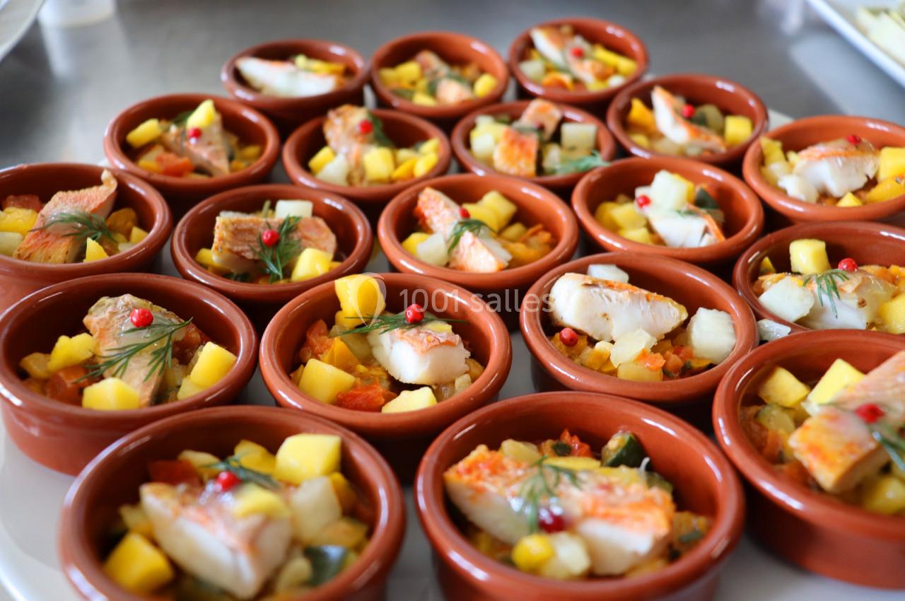 Assortiment de cassolettes en terre cuite garnies de poisson, mangue et légumes colorés, décorées de baies rouges.