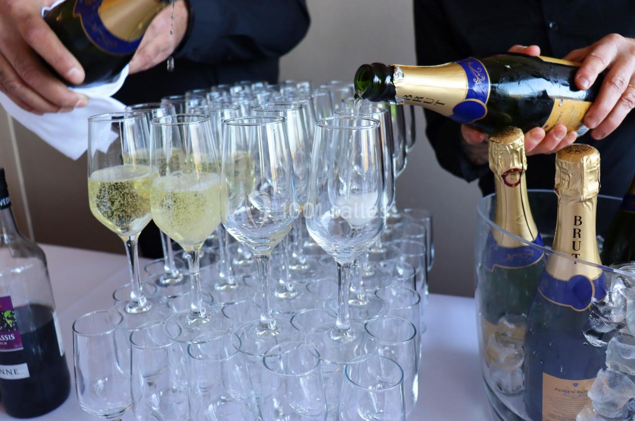 Deux personnes remplissent des flûtes avec du champagne, entourées de bouteilles et d'un seau à glace.