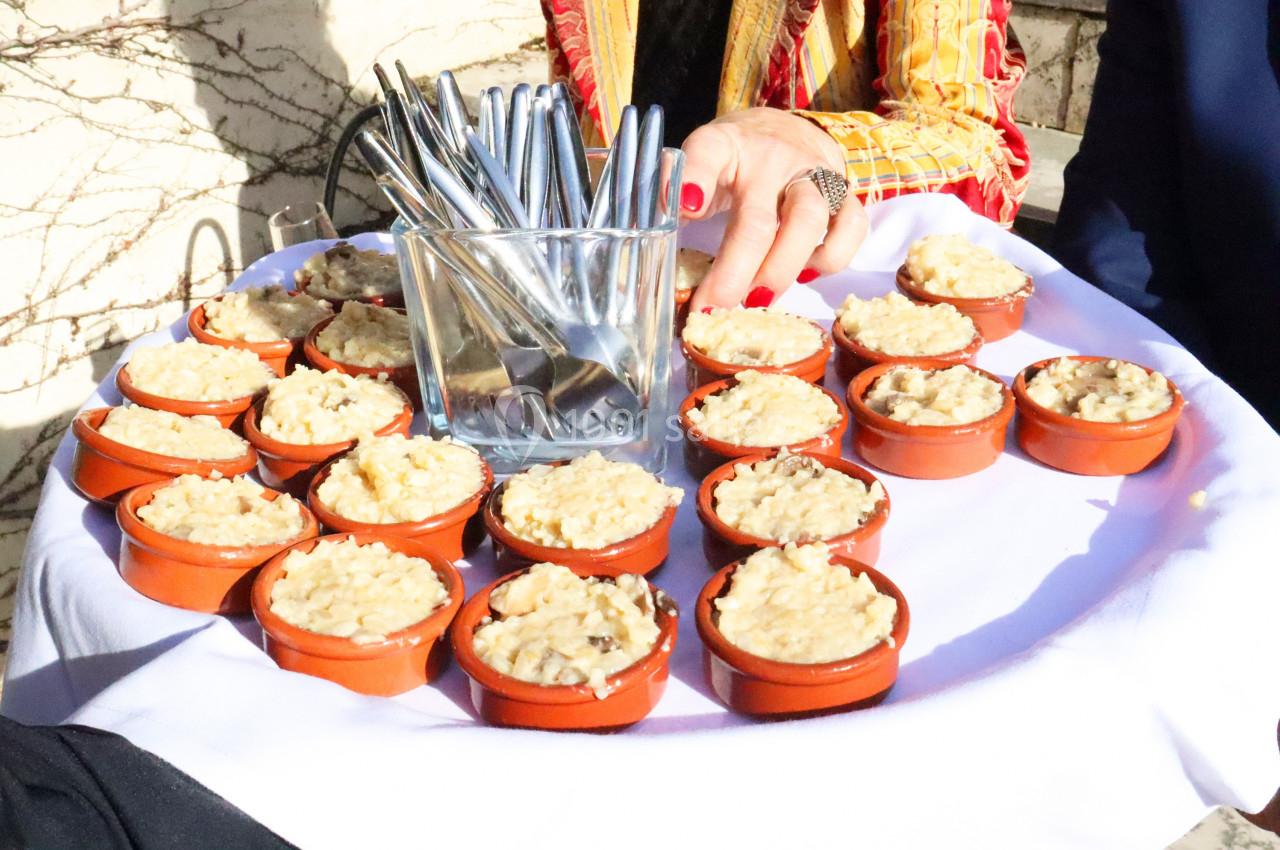 Un plateau de petites cassolettes en terre cuite remplies de gratin, accompagné d'un pot contenant des cuillères.