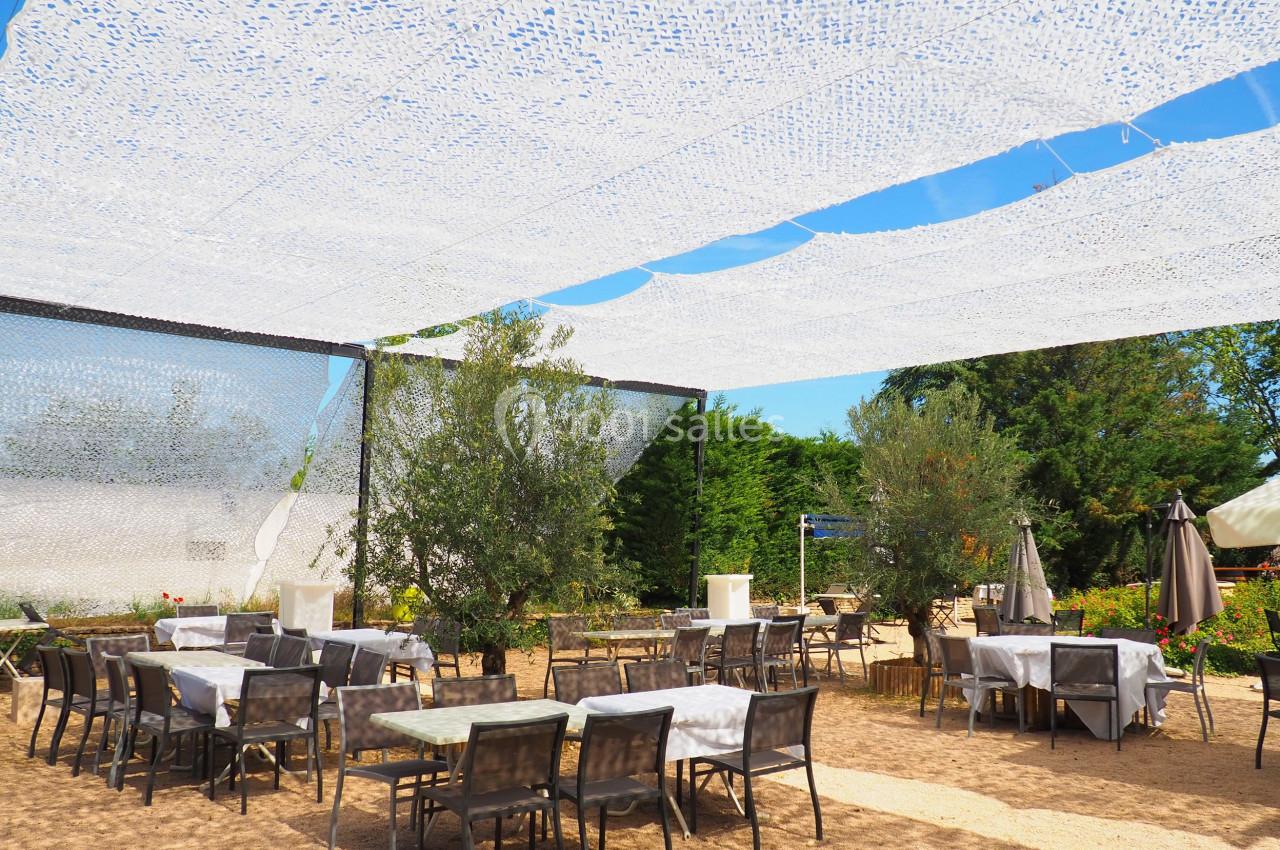 Terrasse extérieure avec tables et chaises sous des voiles d'ombrage blanches, entourée de végétation.