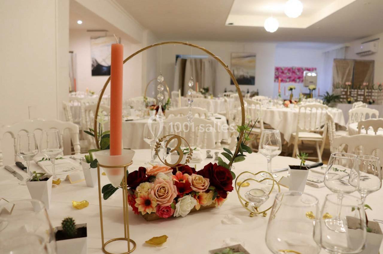 Centre de table floral avec bougie rose et décoration dorée, dans une salle de réception élégamment dressée.