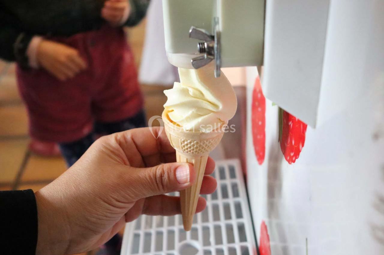 Une main tient un cornet pendant qu'une machine y sert une glace à l'italienne.