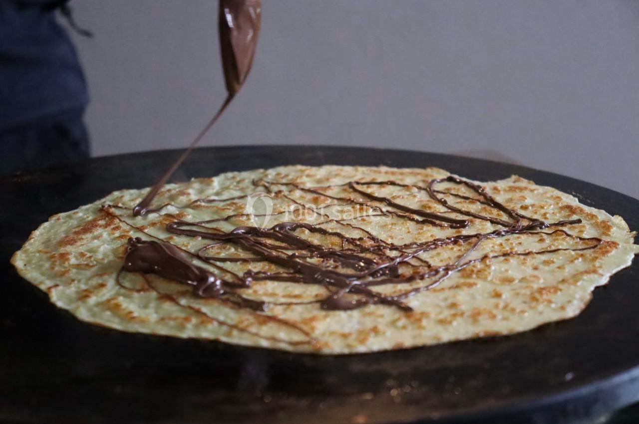 Crêpe en cours de préparation avec du chocolat fondu versé en filet sur une plaque de cuisson.