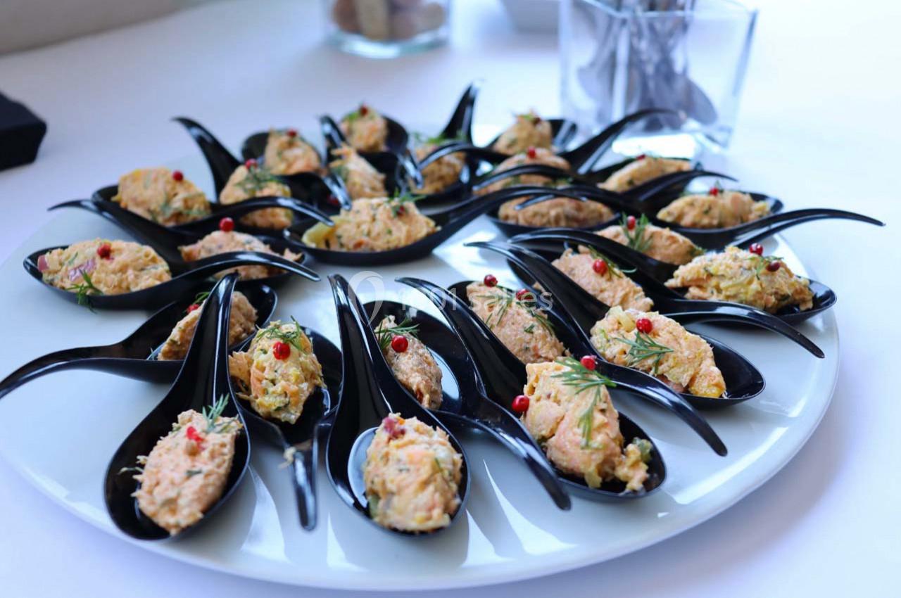 Cuillères noires garnies de bouchées apéritives à base de poisson, décorées de baies rouges et d'herbes fraîches.