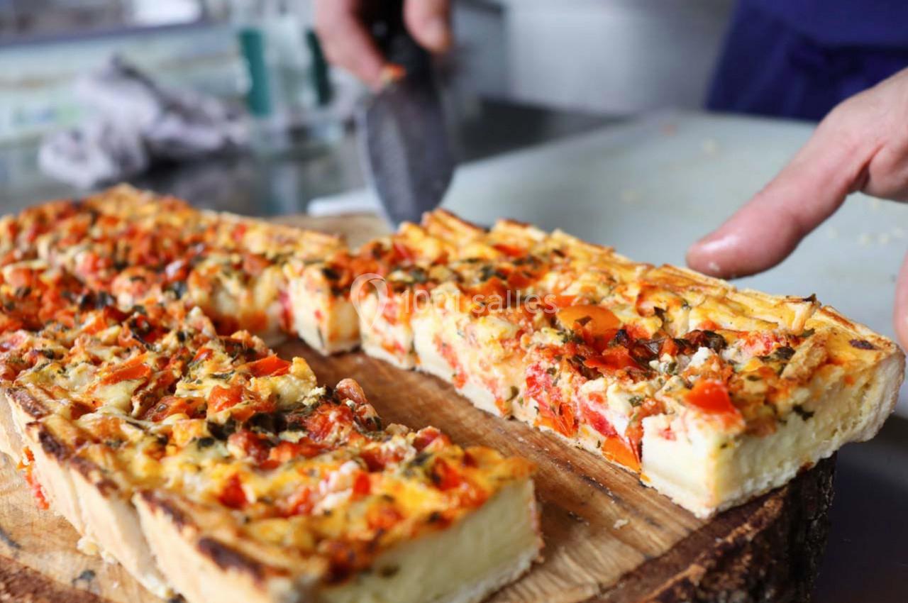 Quiche aux légumes colorés coupée en parts sur une planche en bois, avec une main tenant un couteau.